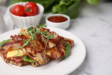 Photo of Tasty sandwich with bacon and microgreens on white marble table, closeup