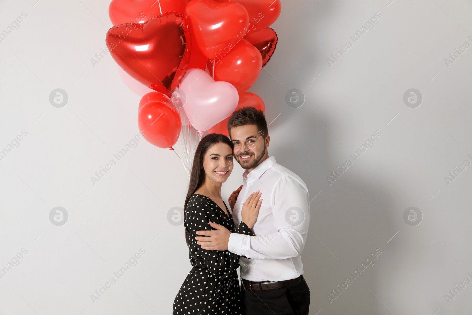 Photo of Happy young couple with heart shaped balloons on light background. Valentine's day celebration