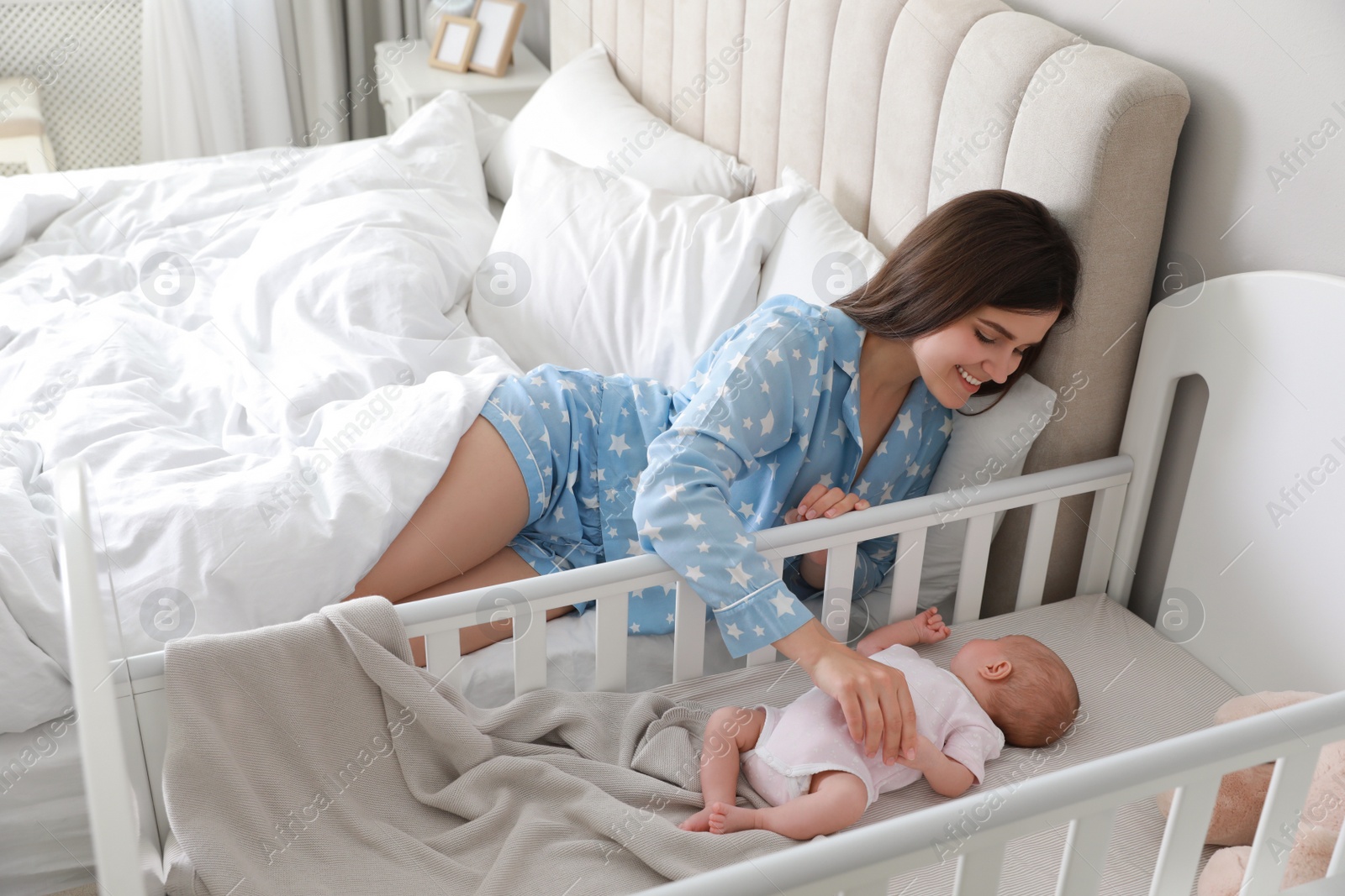 Photo of Happy young mother near bedside crib with her cute newborn baby at home