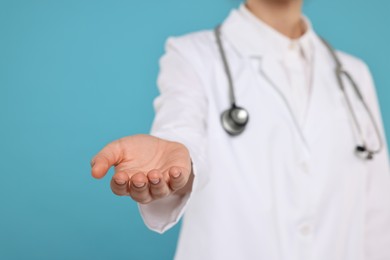 Photo of Doctor with stethoscope holding something on light blue background, closeup