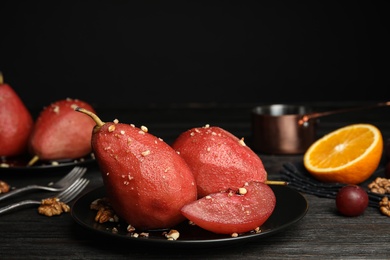 Photo of Plate with red wine poached pears and walnuts on wooden table against black background