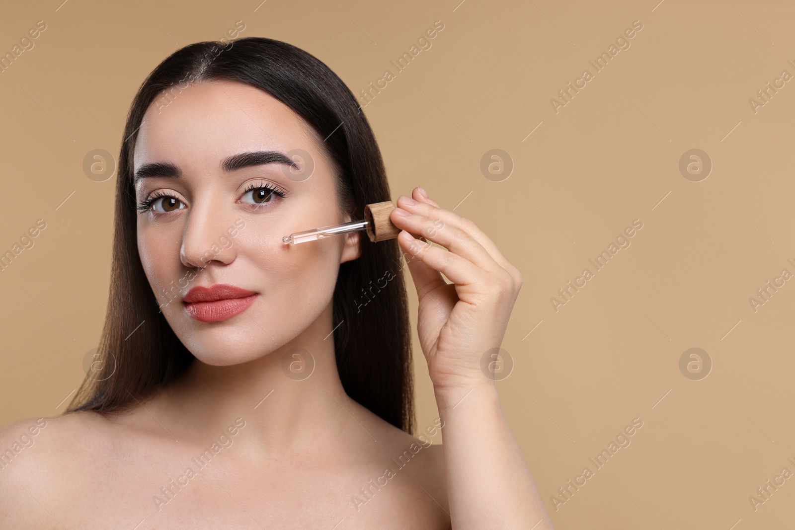 Photo of Young woman applying essential oil onto face on beige background, space for text