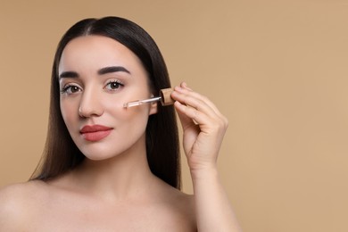 Photo of Young woman applying essential oil onto face on beige background, space for text