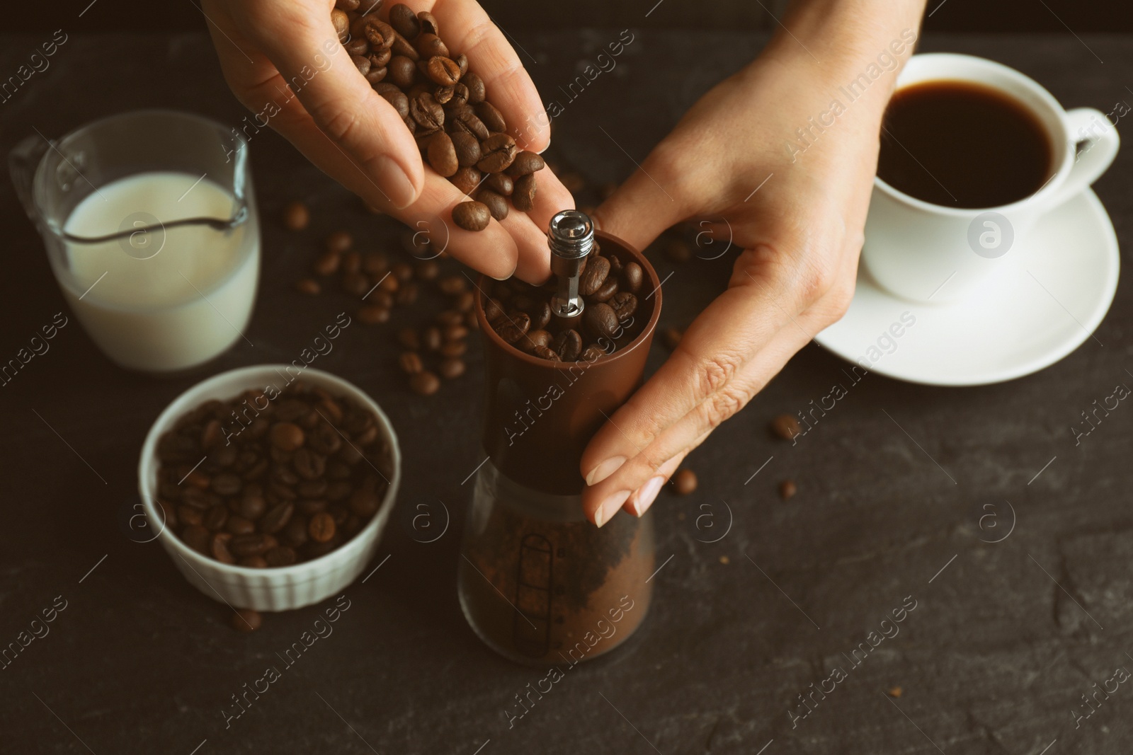 Photo of Woman using manual coffee grinder at black table, closeup