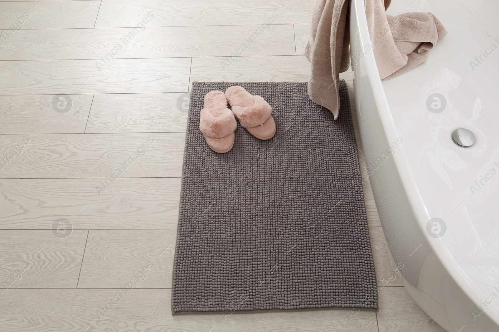 Photo of Soft grey bath mat and slippers on floor in bathroom