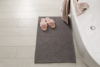 Soft grey bath mat and slippers on floor in bathroom