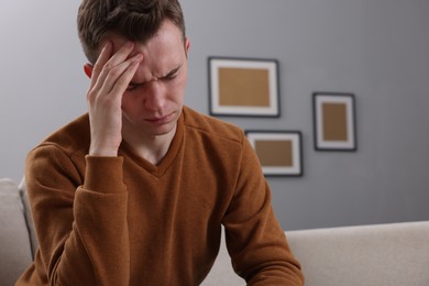 Photo of Sad man suffering from headache on sofa indoors, space for text
