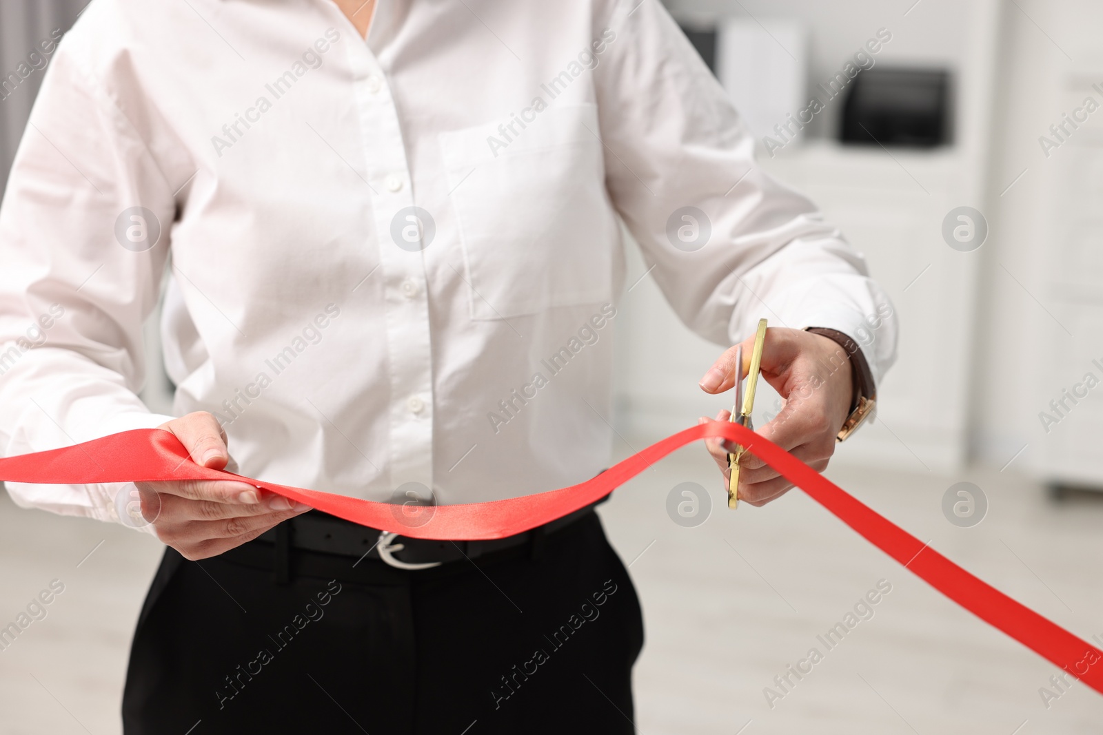 Photo of Woman cutting red ribbon with scissors indoors, closeup