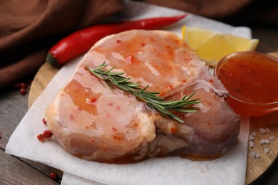 Photo of Board with raw marinated meat, rosemary and spices on wooden table, closeup