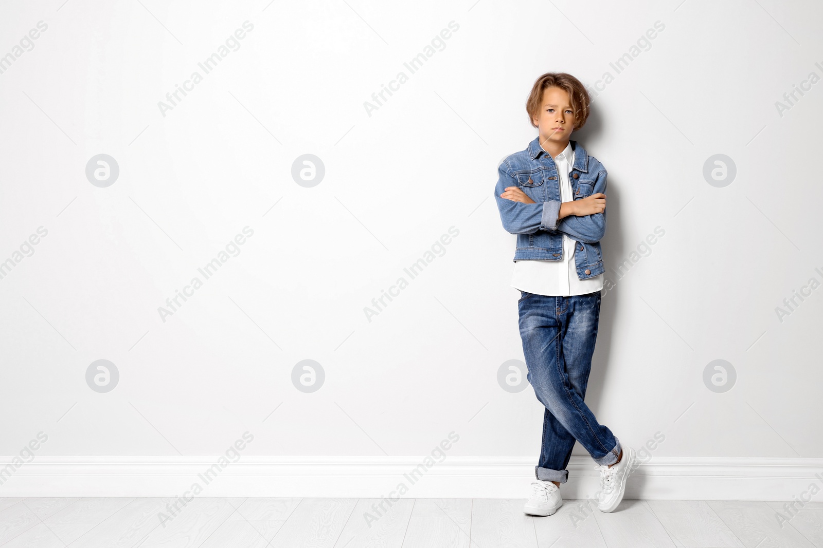 Photo of Cute little boy in casual outfit near white wall. Space for text