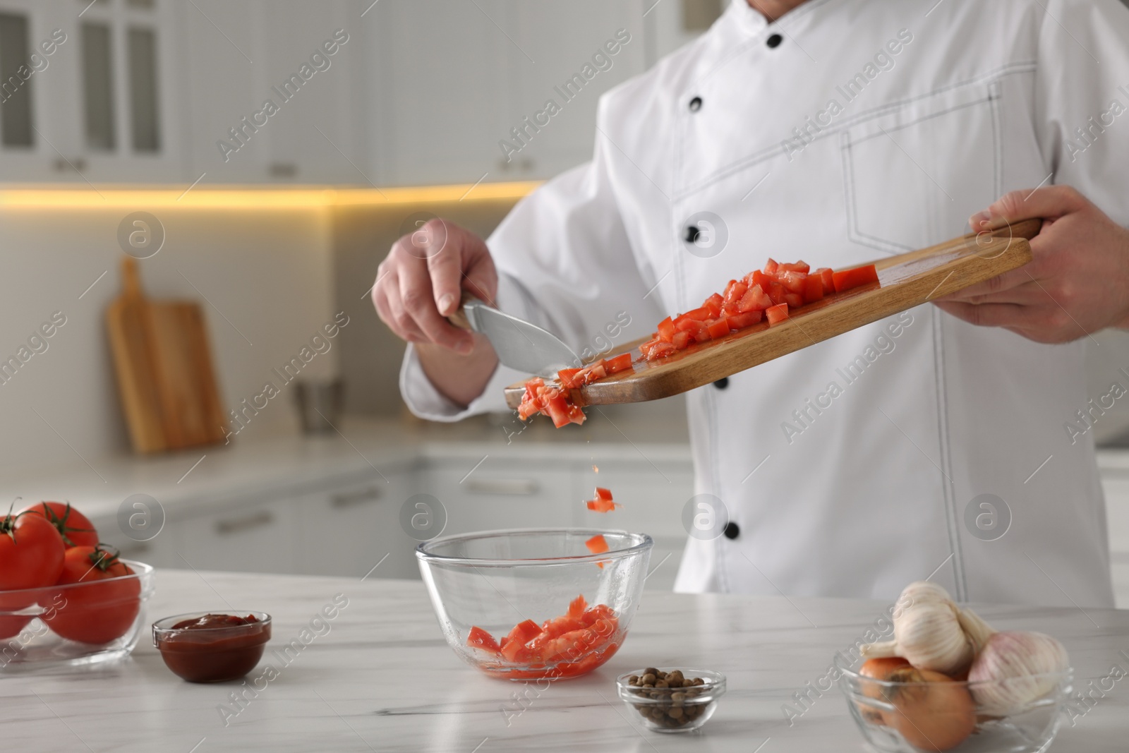 Photo of Professional chef putting cut tomatoes into bowl at white marble table indoors, closeup