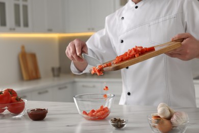 Professional chef putting cut tomatoes into bowl at white marble table indoors, closeup