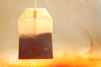 Photo of Brewing tea with bag in hot water, closeup. Space for text