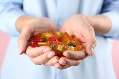 Woman holding handful with delicious gummy fruit shaped candies on pink background, closeup