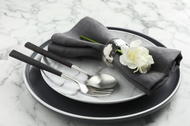 Stylish setting with cutlery, napkin, flowers and plates on white marble table, closeup