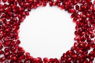 Photo of Frame made of ripe juicy pomegranate grains on white background, top view. Space for text