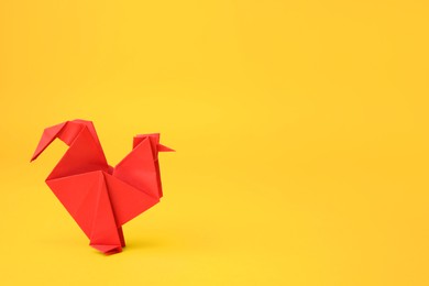 Photo of Origami art. Handmade red paper rooster on yellow background, space for text