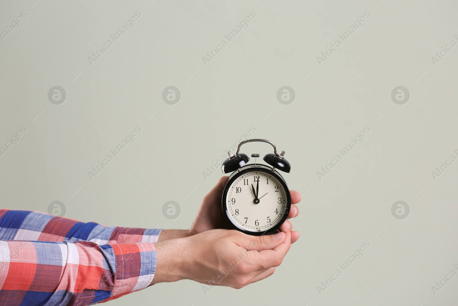 Photo of Young man holding alarm clock on grey background. Time concept