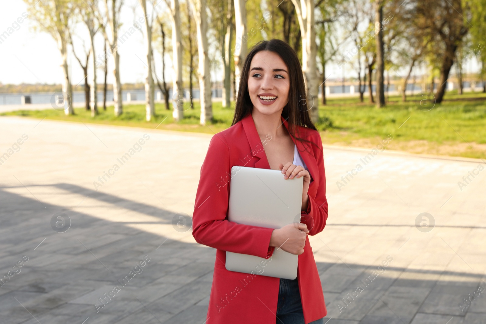 Image of Happy young woman with laptop walking outdoors