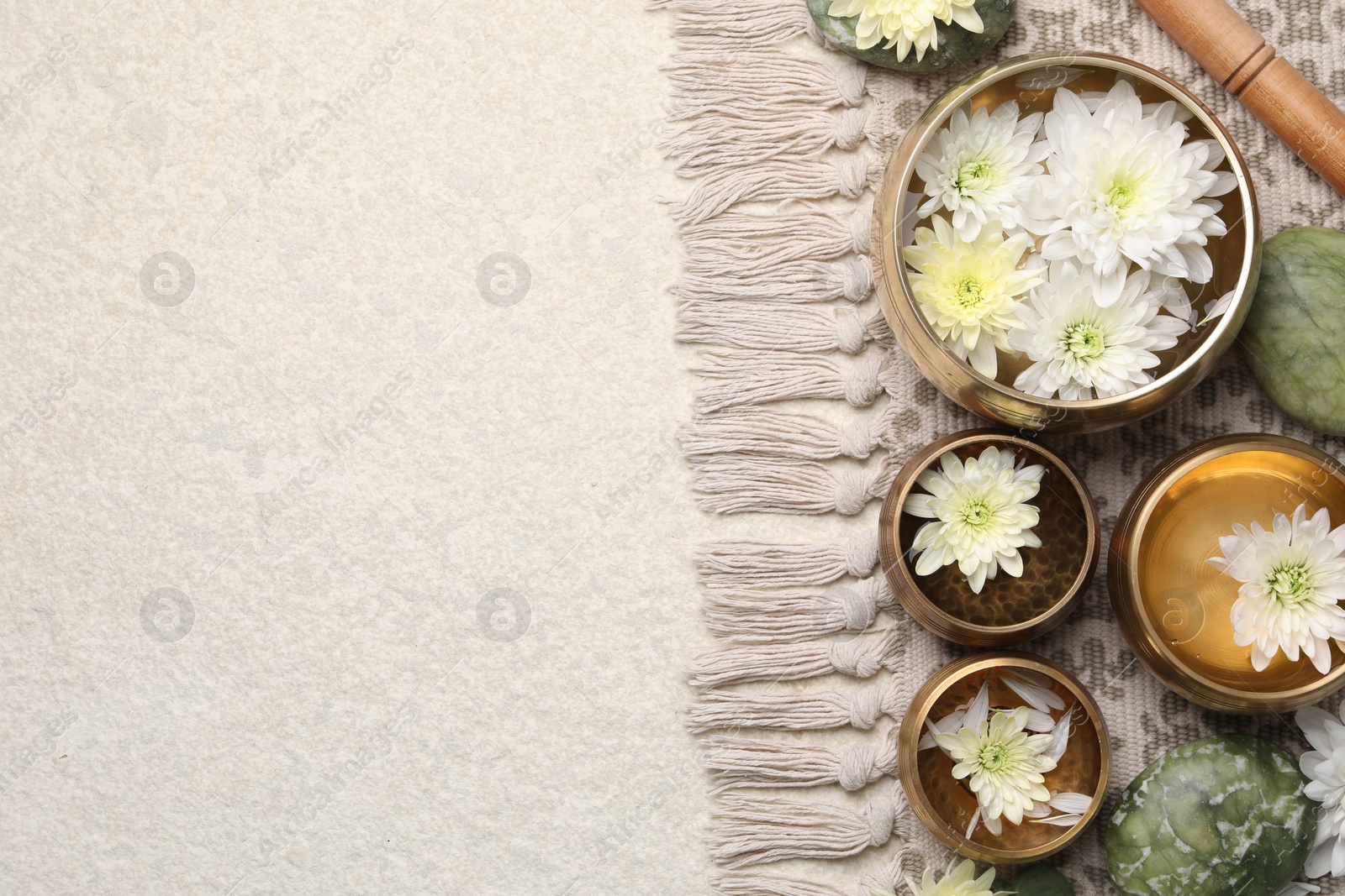 Photo of Tibetan singing bowls with beautiful chrysanthemum flowers, mallet and stones on table, flat lay. Space for text