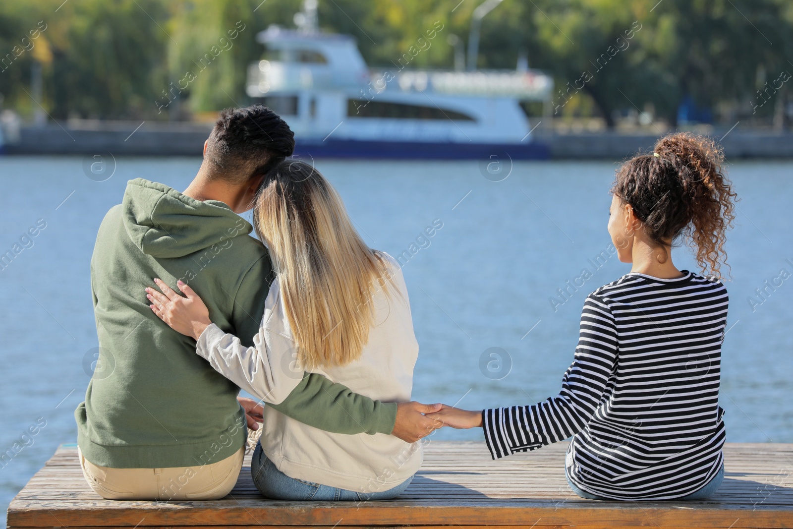 Photo of Man holding hands with another woman behind his girlfriend's back on pier near river. Love triangle