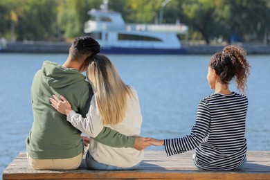 Photo of Man holding hands with another woman behind his girlfriend's back on pier near river. Love triangle