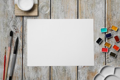 Flat lay composition with blank paper sheet and watercolor paints on light grey wooden table