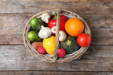 Photo of Basket with ripe fruits and vegetables on wooden table, top view