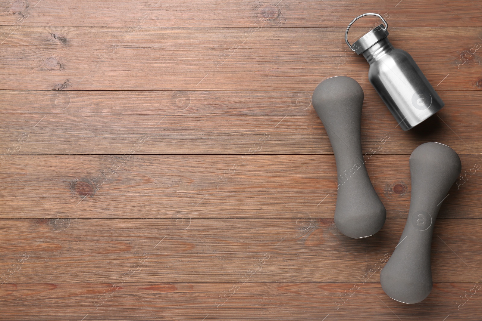 Photo of Dumbbells and metal water bottle on wooden table, flat lay. Space for text