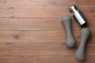 Dumbbells and metal water bottle on wooden table, flat lay. Space for text