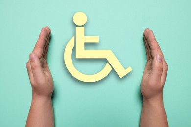 Image of Disability inclusion. Woman protecting wheelchair symbol on turquoise background, closeup