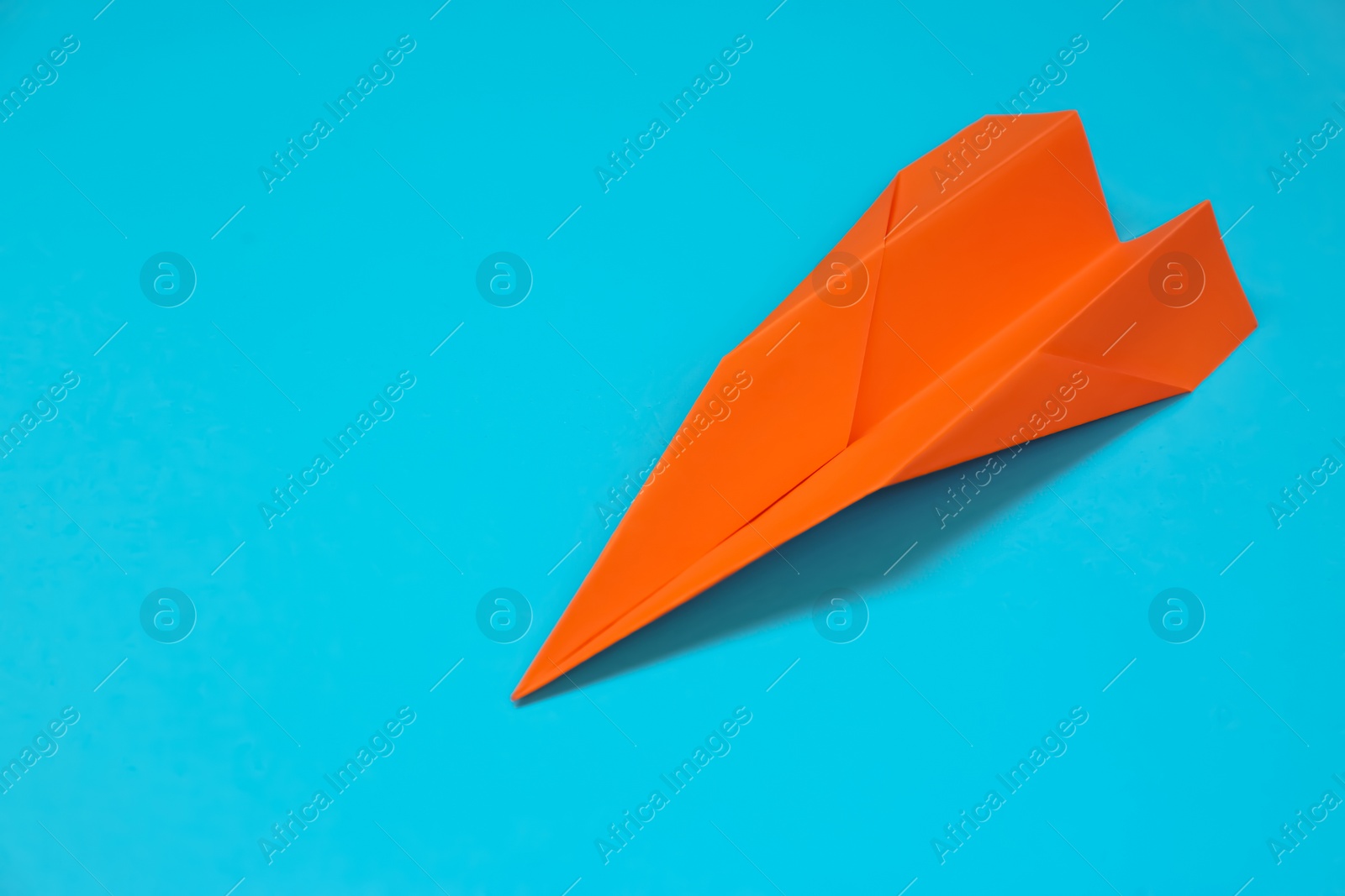 Photo of Orange paper plane on light blue background, space for text
