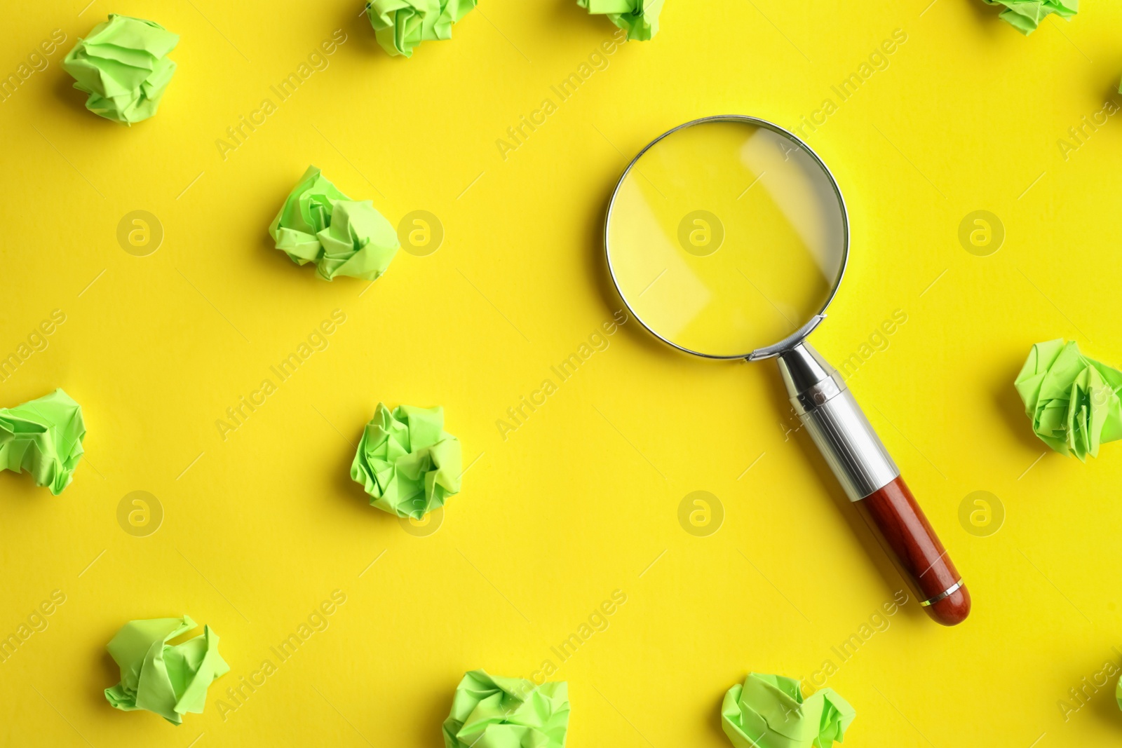 Photo of Magnifier glass and green crumpled paper sheets on yellow background, flat lay. Find keywords concept