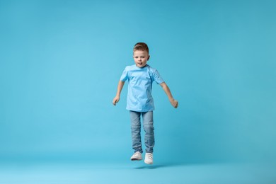 Happy little boy dancing on light blue background