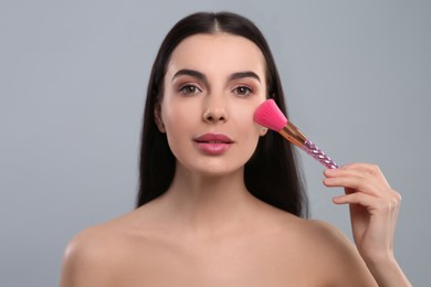 Photo of Woman applying makeup with brush on light grey background