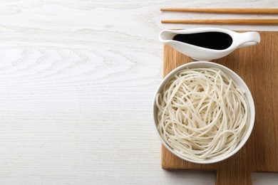 Photo of Bowl of rice cooked noodles and soy sauce served on white wooden table, flat lay. Space for text