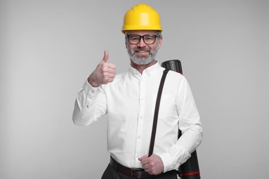 Photo of Architect in hard hat with drawing tube showing thumb up on grey background