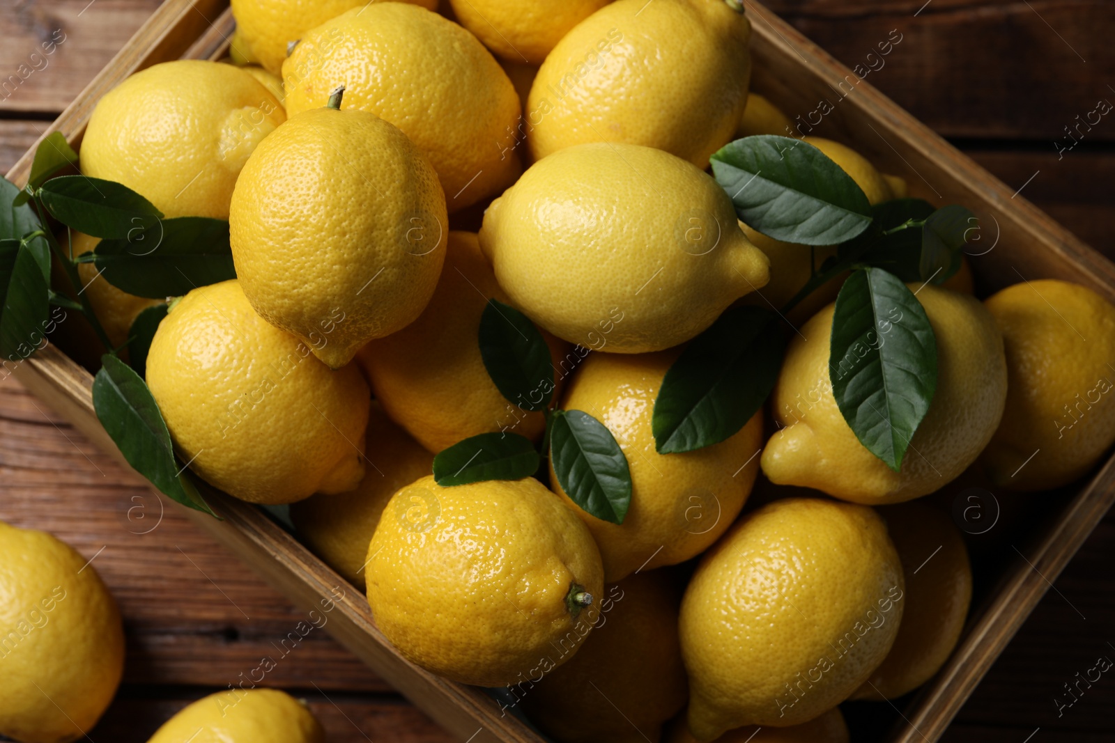 Photo of Fresh lemons in crate on wooden table, top view