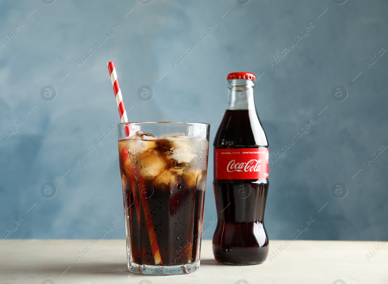 Photo of MYKOLAIV, UKRAINE - NOVEMBER 15, 2018: Bottle and glass with Coca Cola on table against color background