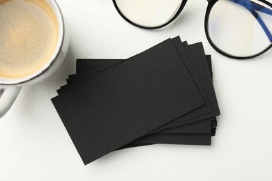 Photo of Blank black business cards, glasses and cup of coffee on white table, flat lay. Mockup for design