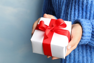 Young woman holding Christmas gift on blue background, closeup