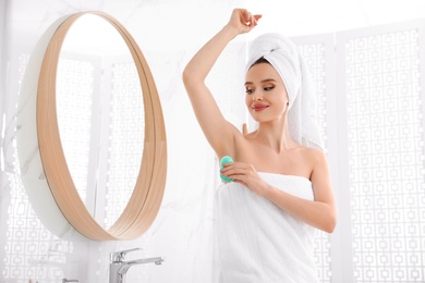 Photo of Beautiful young woman applying deodorant after shower in bathroom