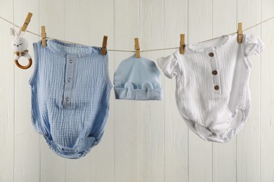 Photo of Baby clothes and accessories hanging on washing line near white wooden wall