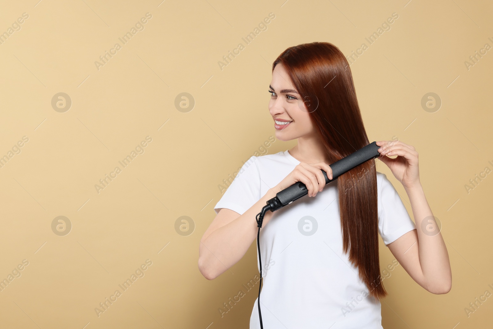 Photo of Beautiful woman using hair iron on beige background, space for text