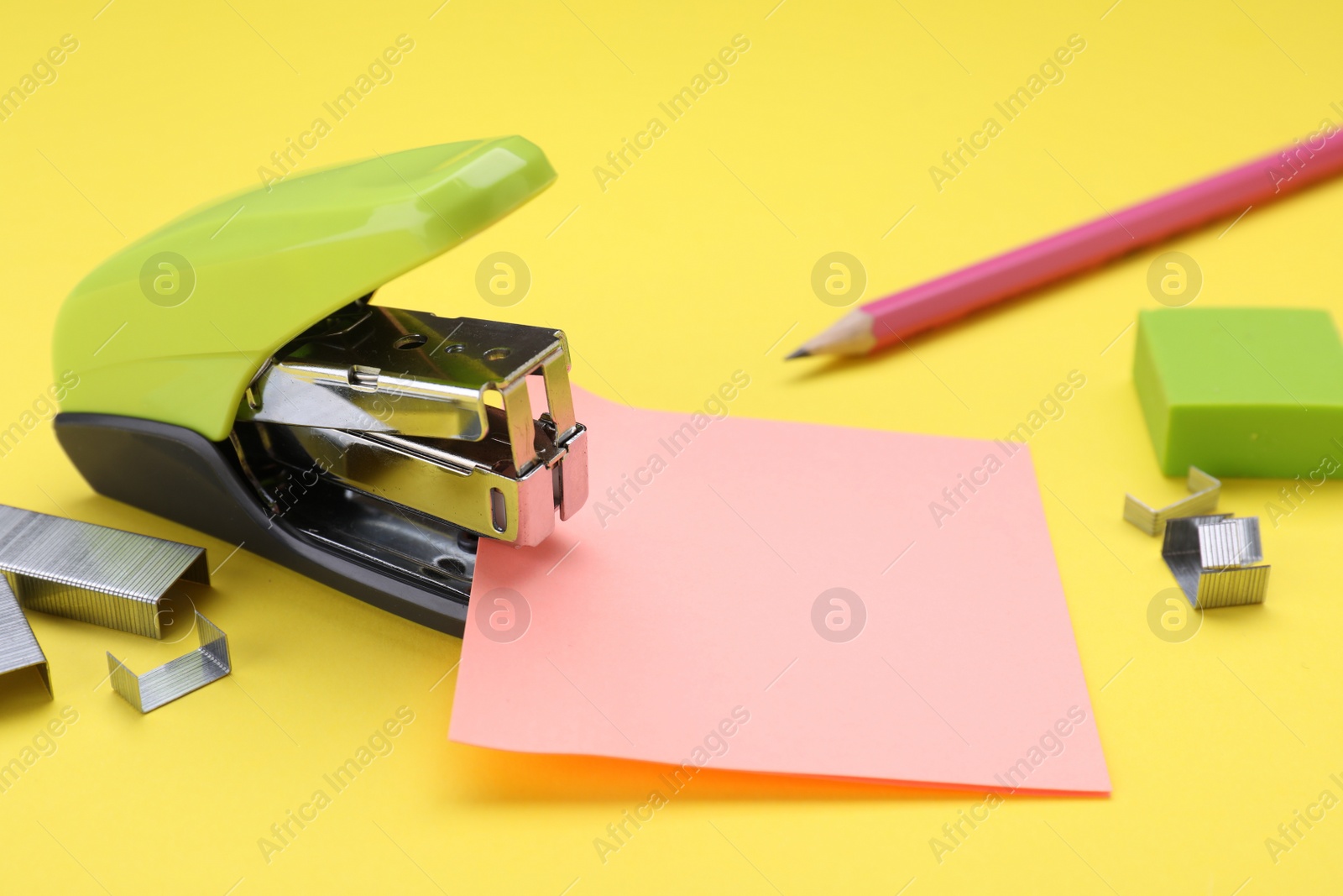 Photo of New bright stapler with staples and sticky notes on yellow background. School stationery