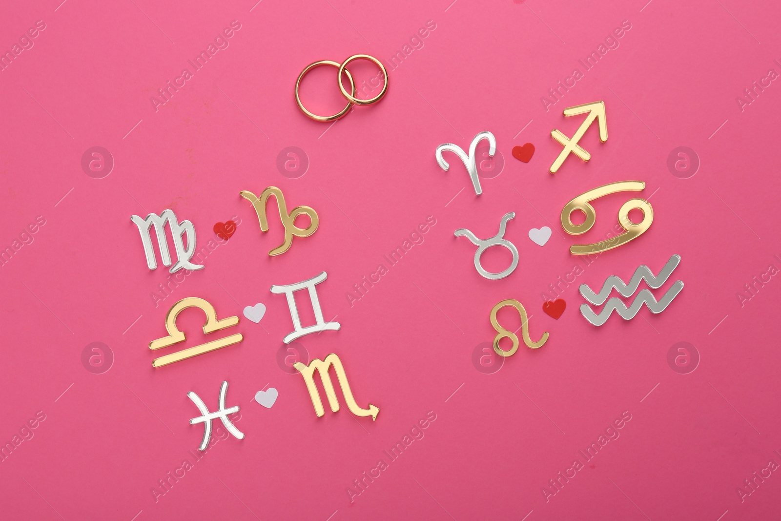 Photo of Zodiac compatibility. Signs and wedding rings on pink background, flat lay