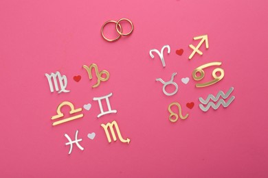 Zodiac compatibility. Signs and wedding rings on pink background, flat lay