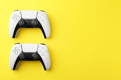 Wireless game controllers on yellow background, flat lay. Space for text