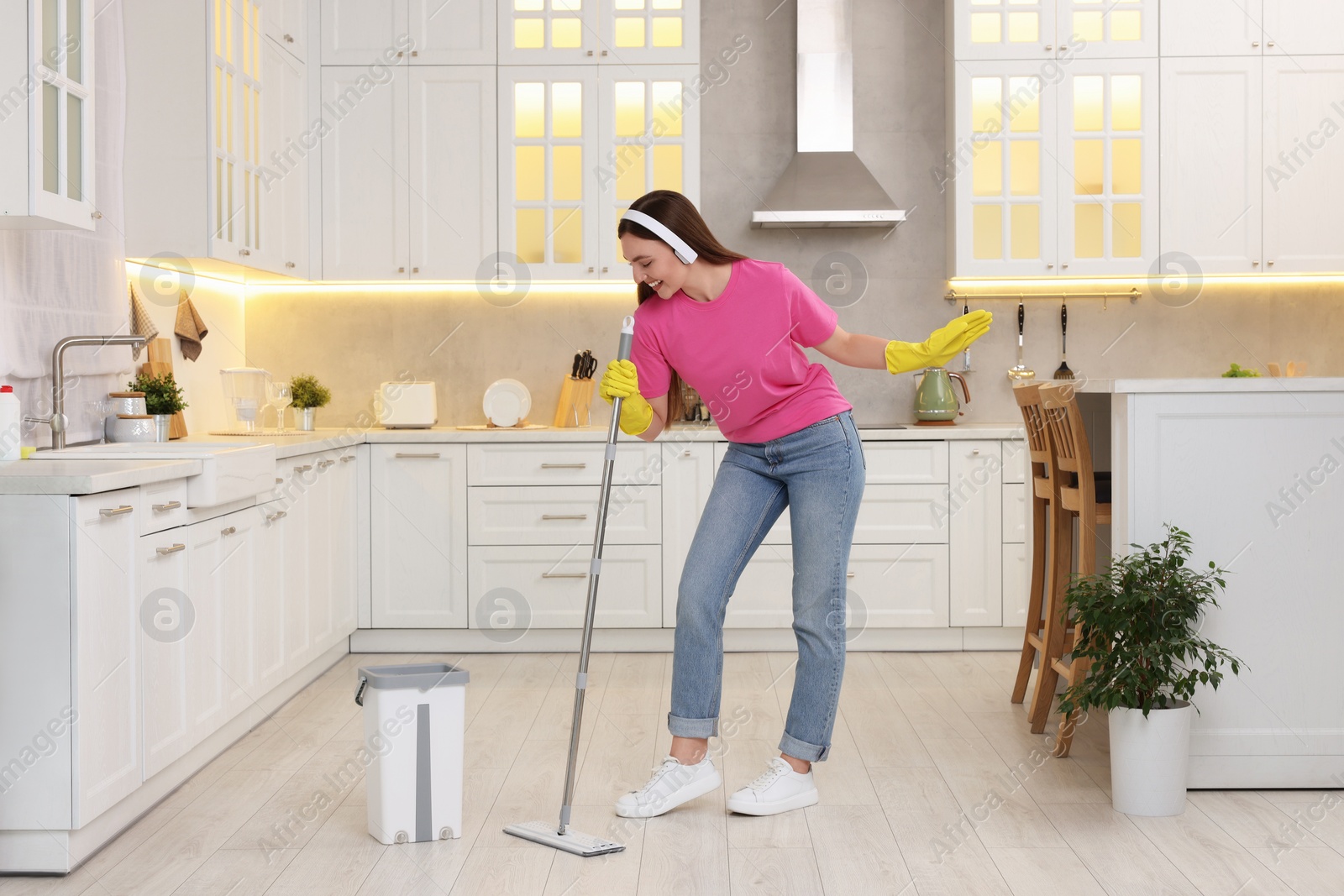 Photo of Enjoying cleaning. Happy woman with mop singing while tidying up in kitchen