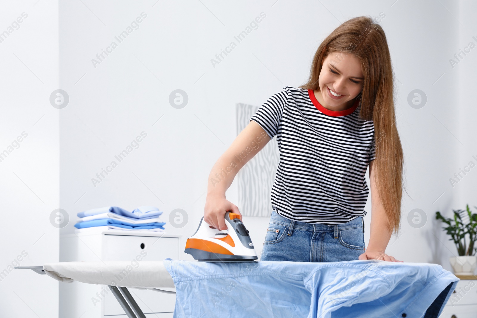 Photo of Young woman ironing clothes on board at home. Space for text